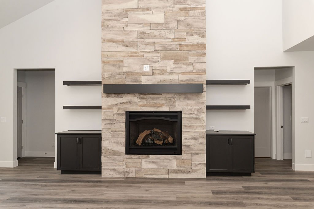 Living room with a modern fireplace, stone wall, black cabinets on sides, and floating shelves, with hardwood flooring and archways on either side.