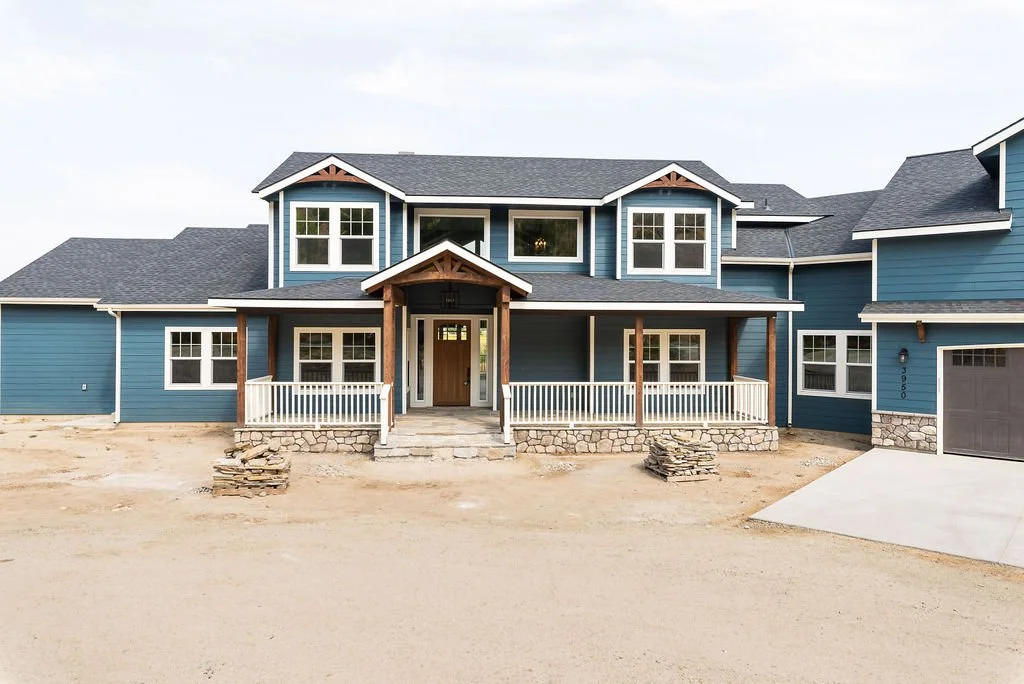 New blue two-story house under construction with a front porch, stone foundation, and a concrete driveway.