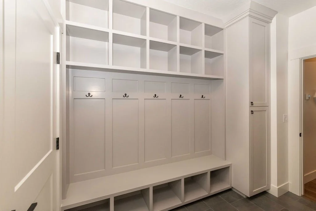 White built-in entryway storage with cubbies, hooks, and overhead shelves in a modern home.