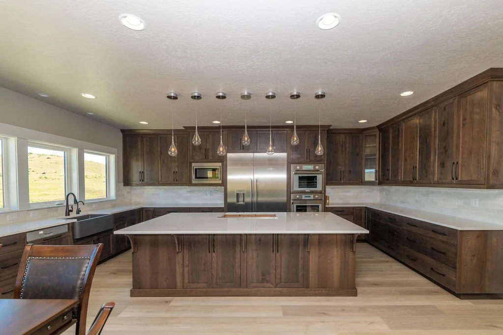 Modern kitchen with wooden cabinets, stainless steel appliances, white countertops, and pendant lights.