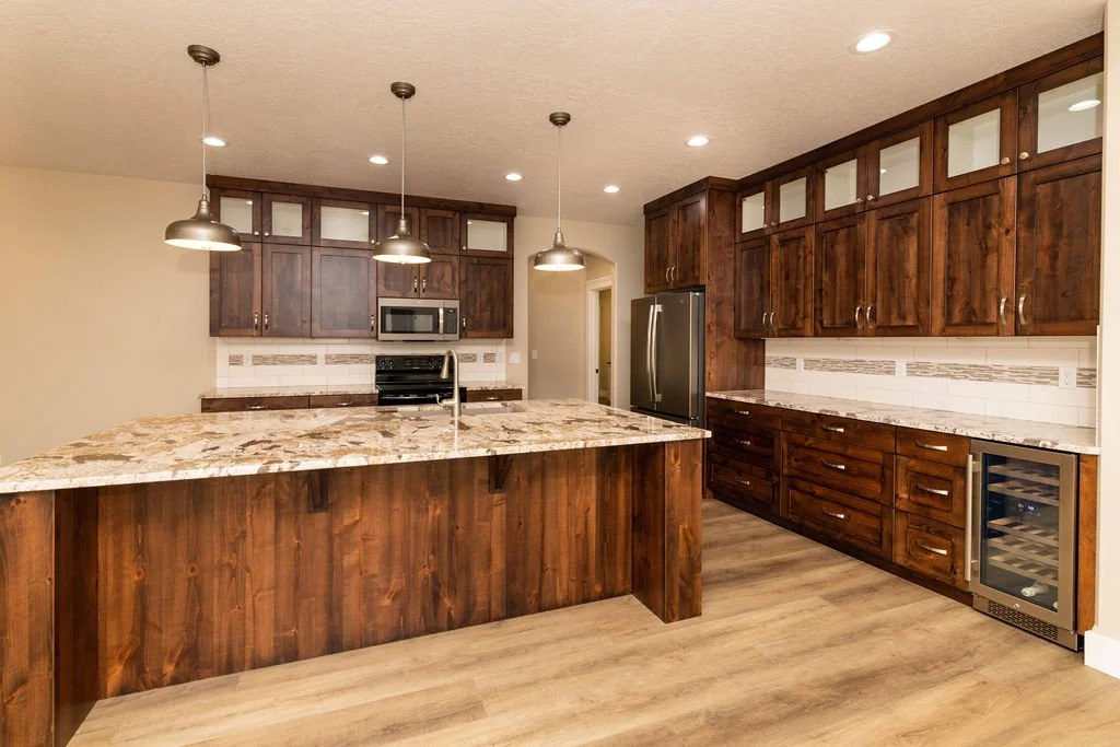 Modern kitchen with wooden cabinets, a large granite kitchen island, stainless steel appliances, and pendant and recessed lighting.