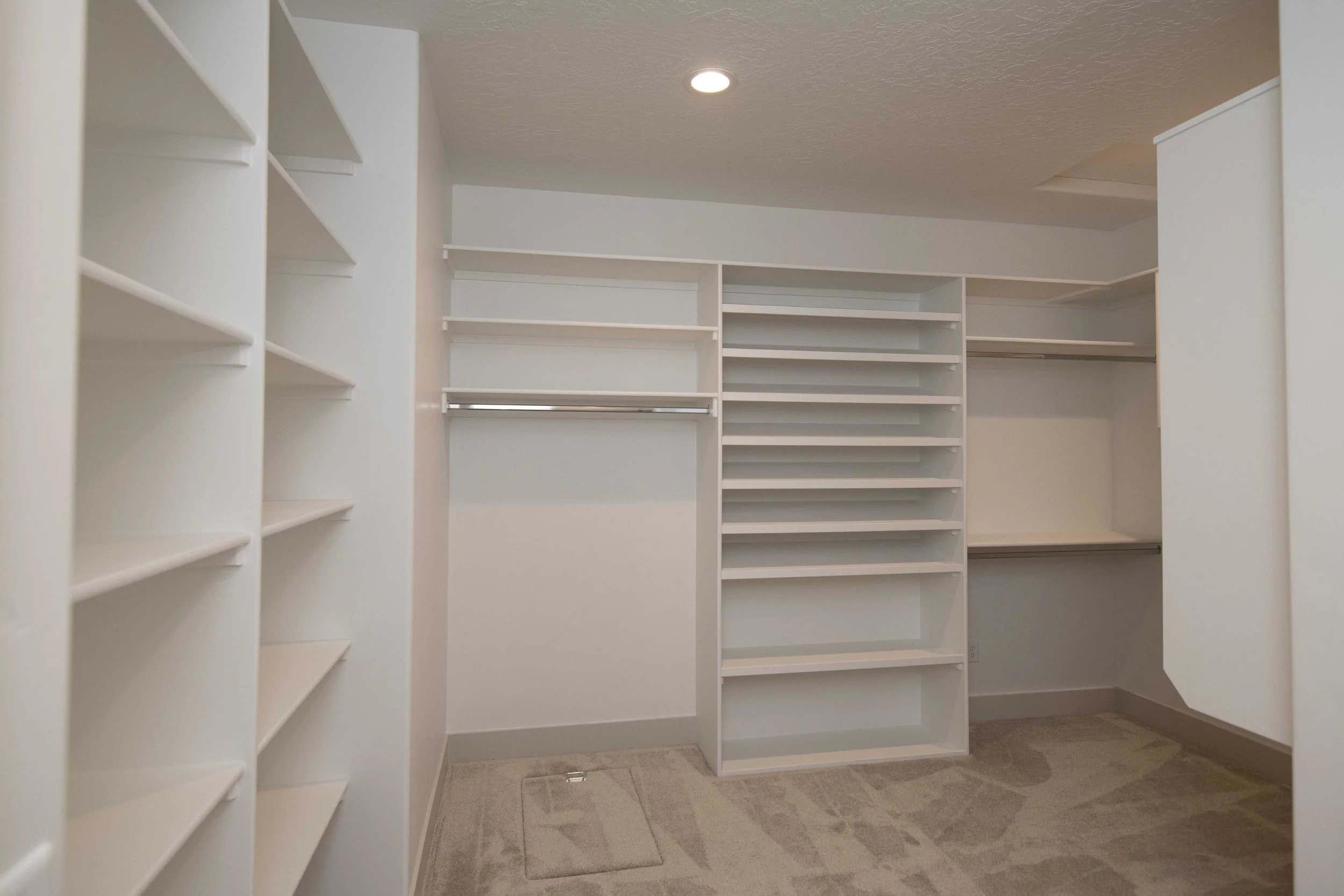 Empty white walk-in closet with multiple shelves and hanging rods, carpeted floor, ceiling recessed lighting.