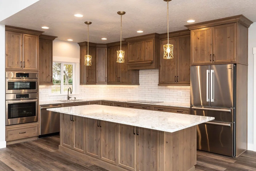 Modern kitchen with wooden cabinets, white backsplash, granite island, stainless steel appliances, and pendant lighting.