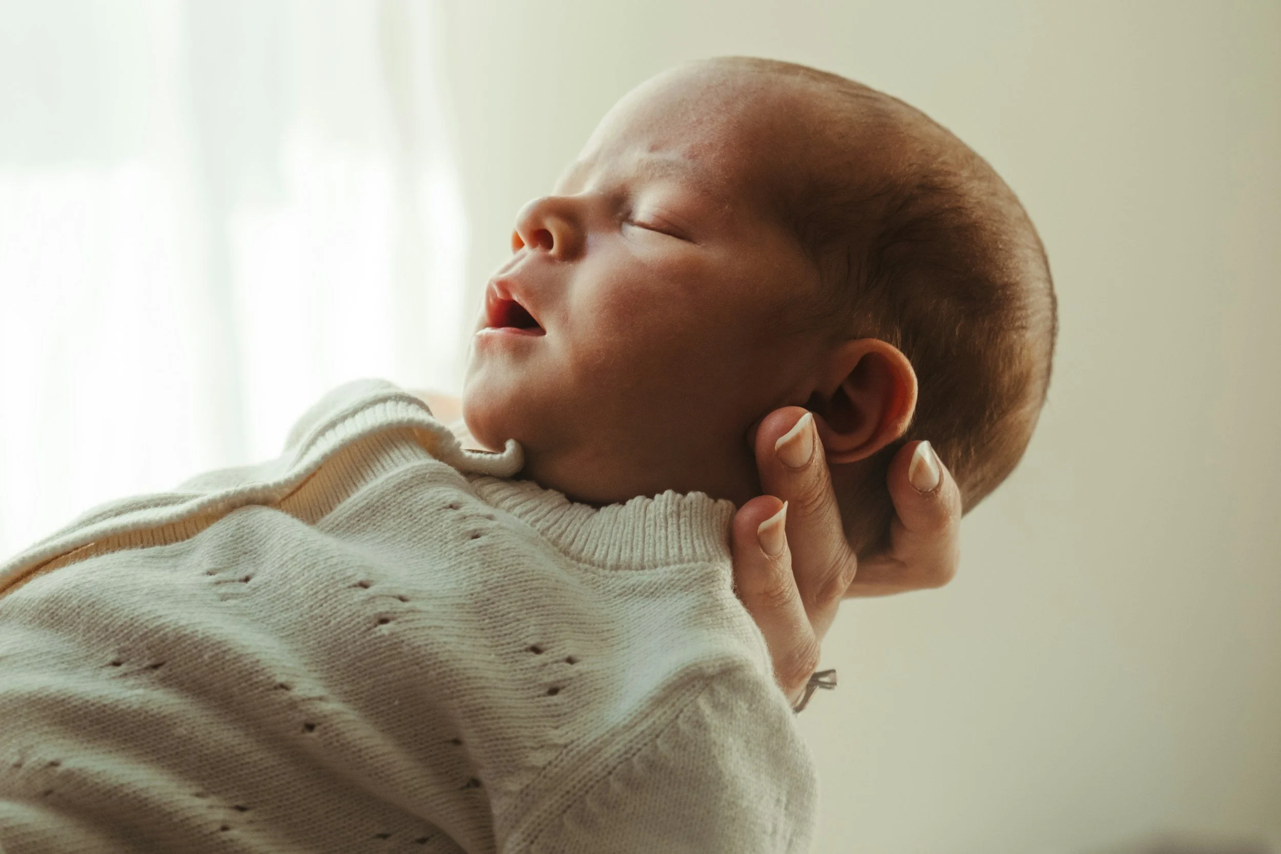 Close-up of a sleeping baby with smooth skin and sparse hair, being gently held by an adult hand.