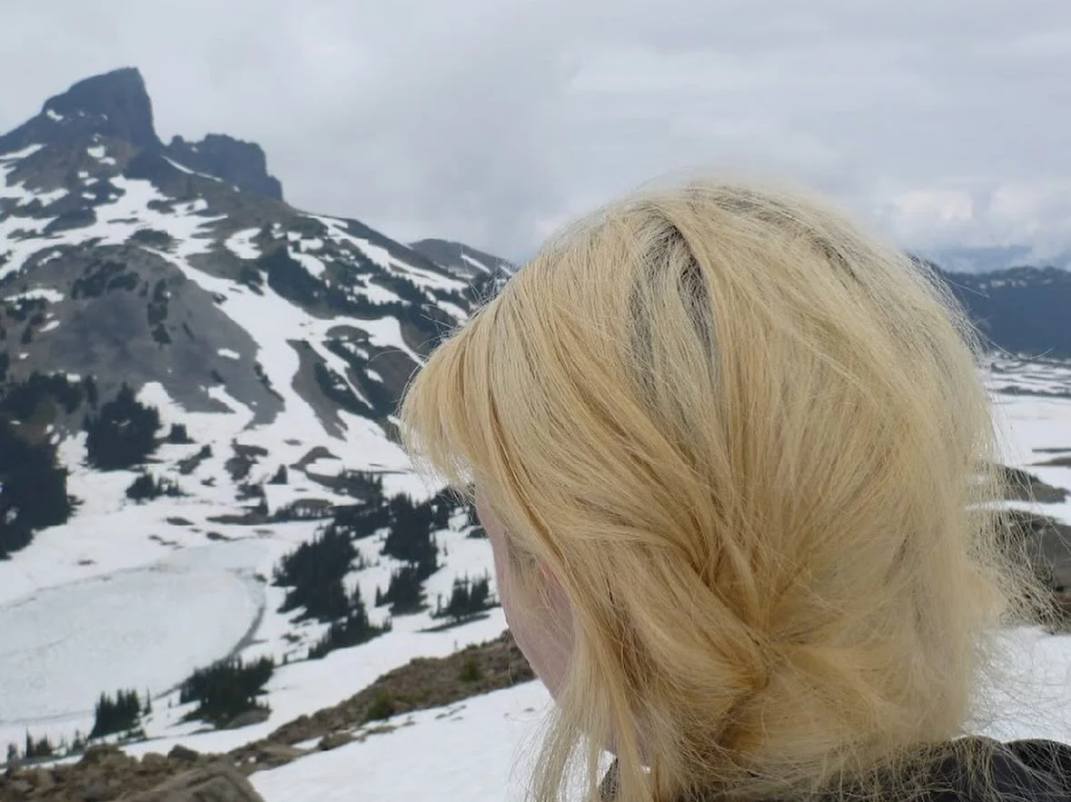 Person with blonde hair looking at snow-covered mountainous landscape.