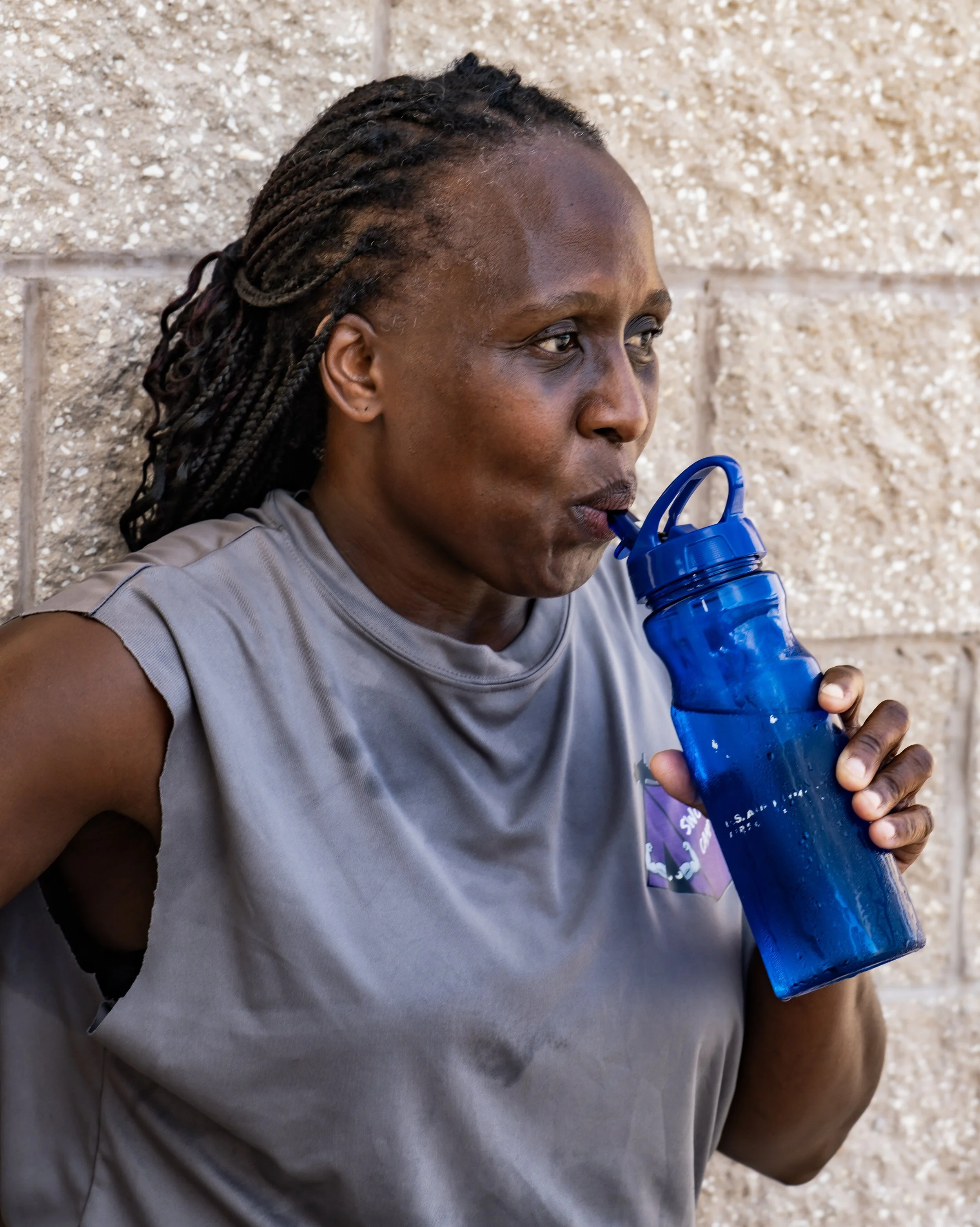 A woman with braided hair drinking from a blue water bottle.