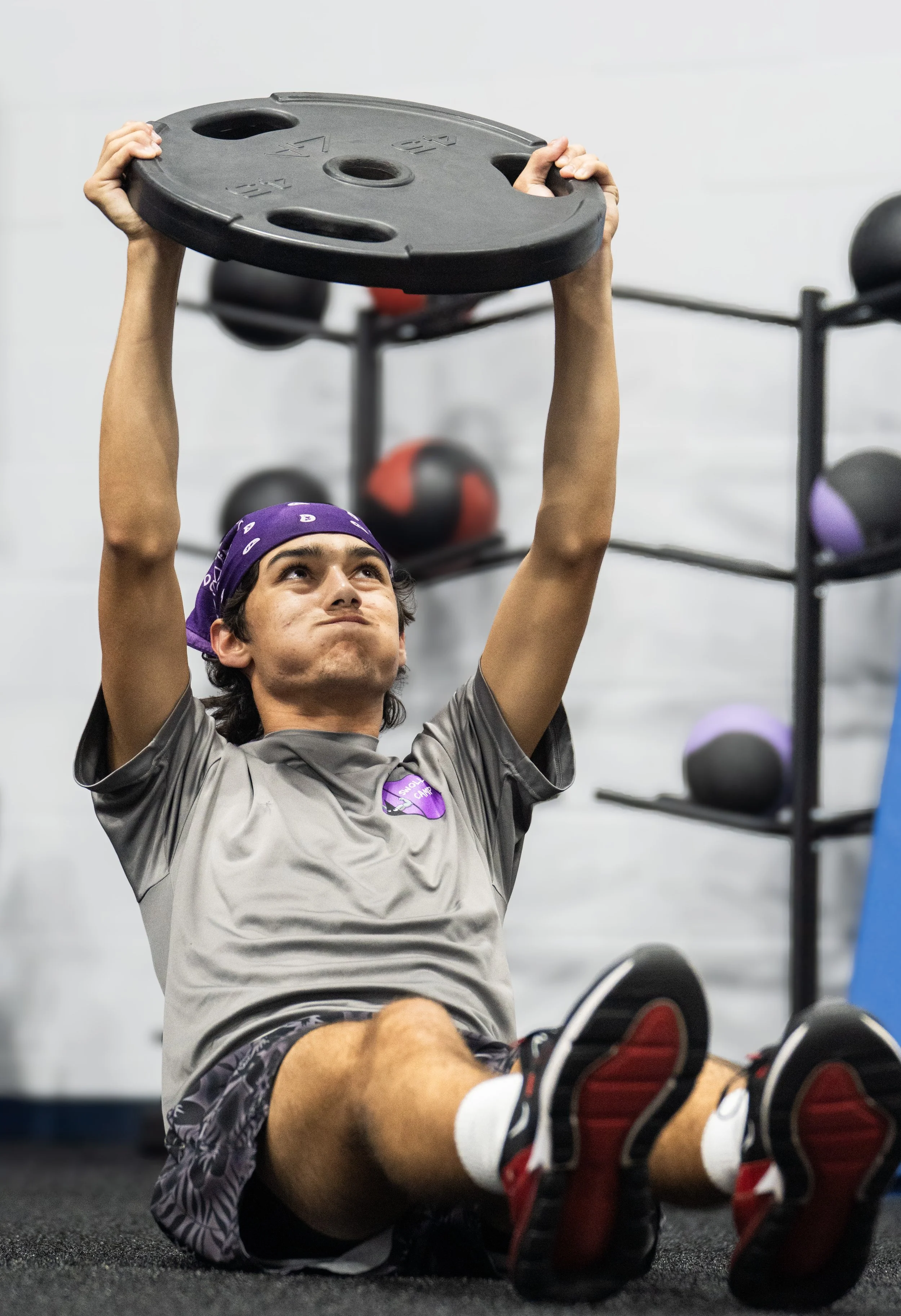 A person with a purple bandana lifting a weight plate during a workout at the gym.