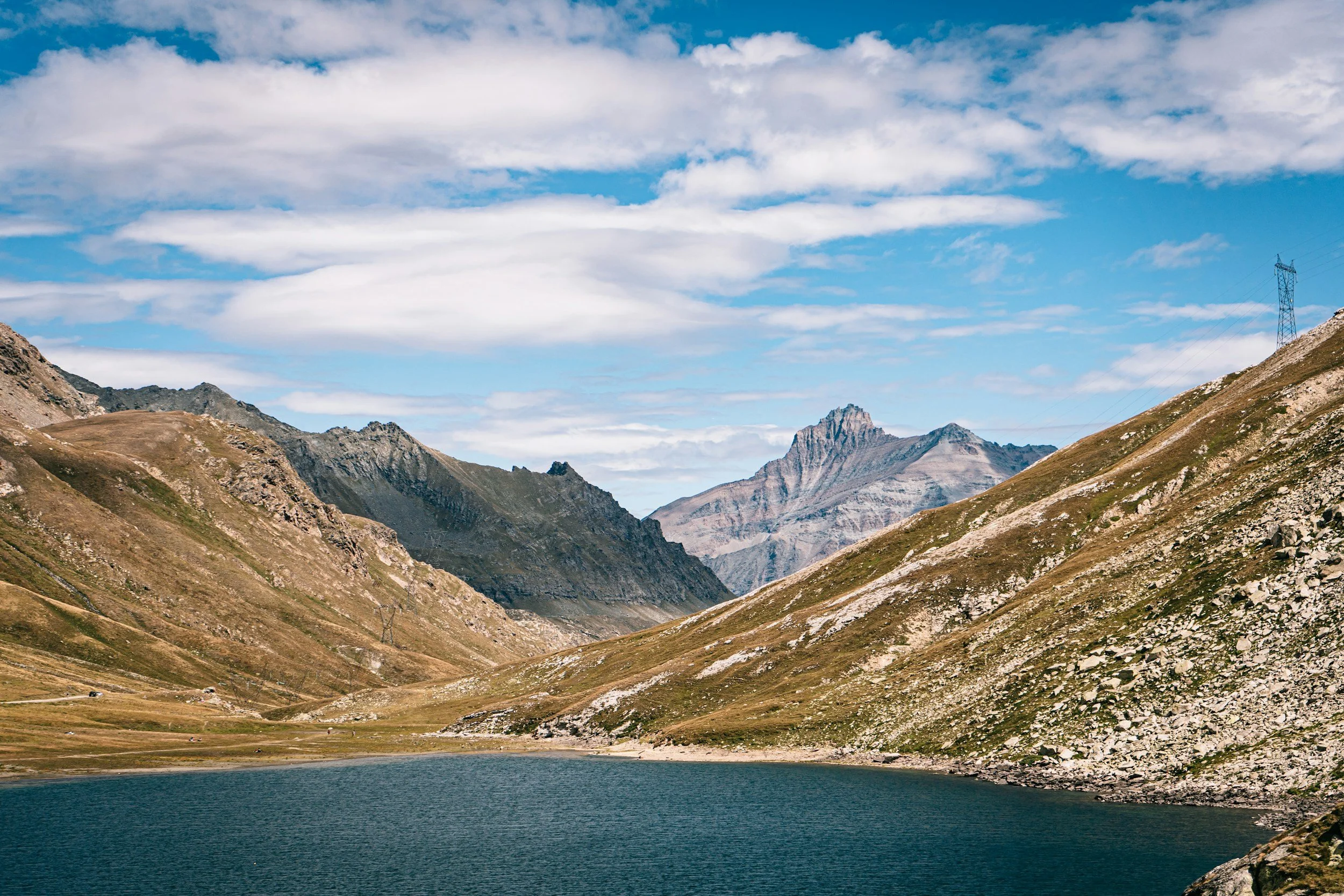 Mountain landscape with a lake in the foreground, rugged mountains in the background, and partly cloudy sky.
