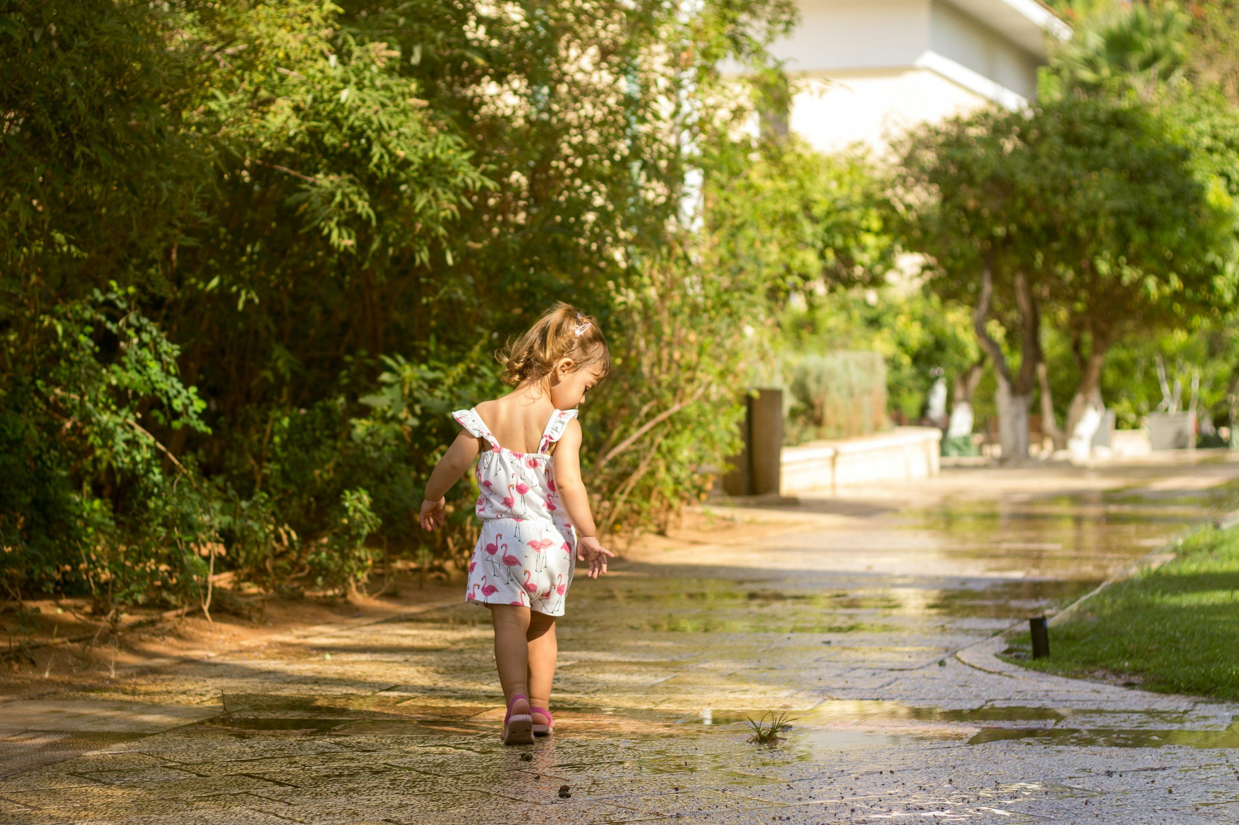 A young girl walking down a paved path lined with greenery on a sunny day.