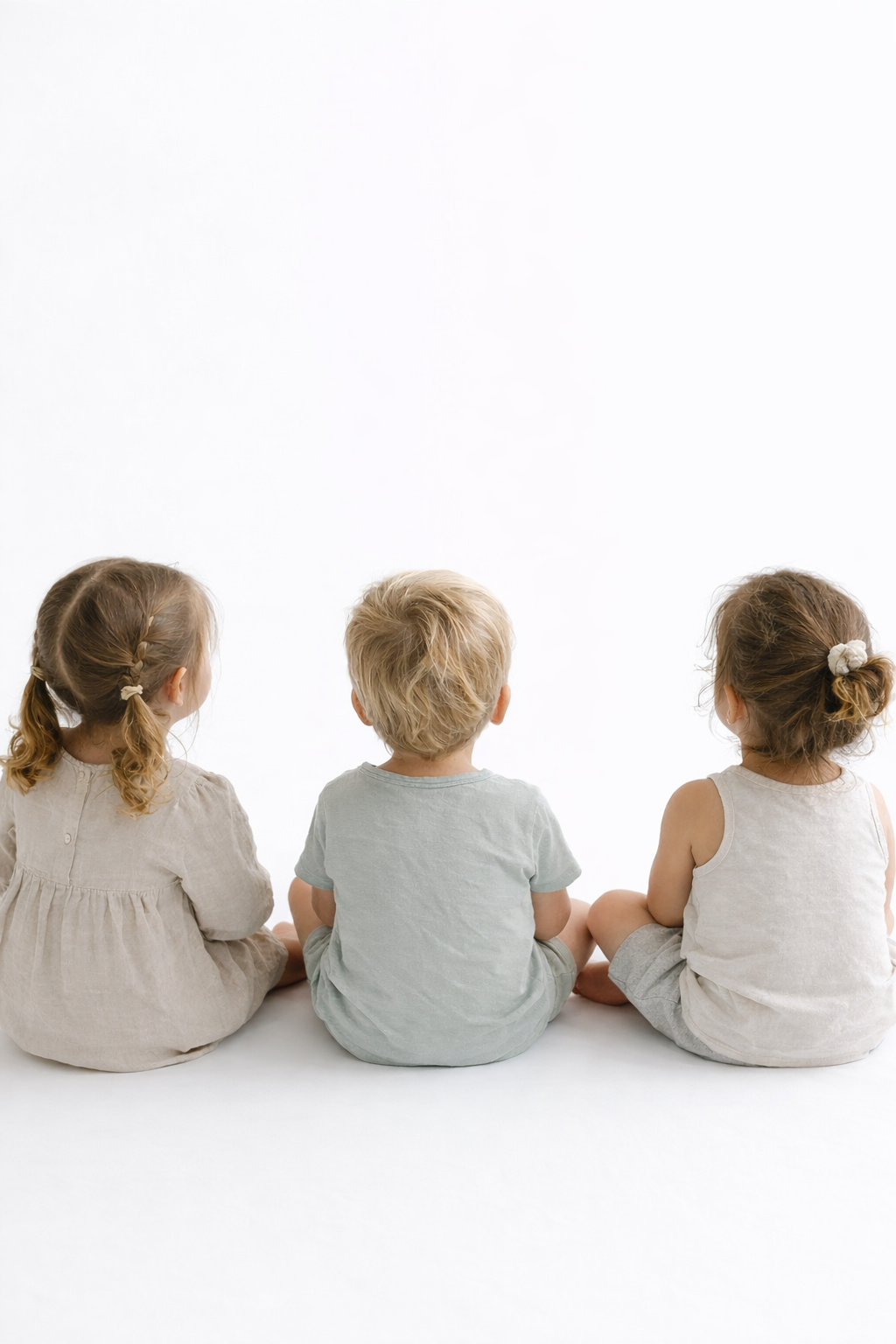 Three young children sitting on the floor, facing away, against a plain white background.