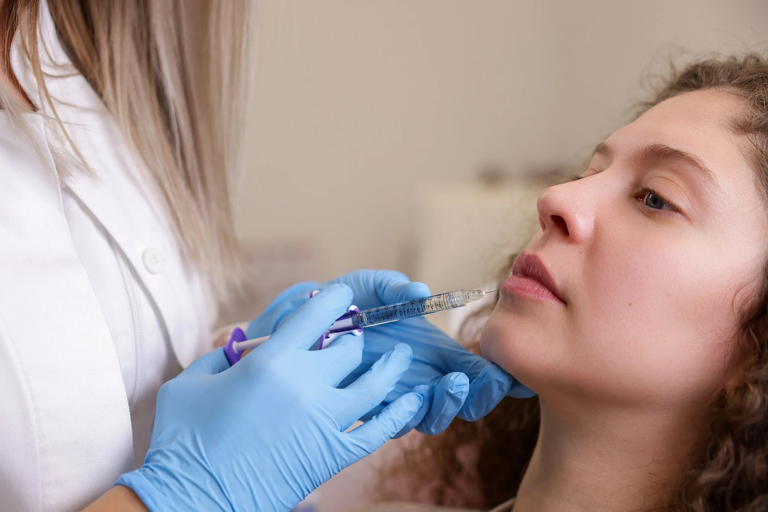 A nurse wearing blue gloves preparing a young woman for an injection or vaccination with a syringe.