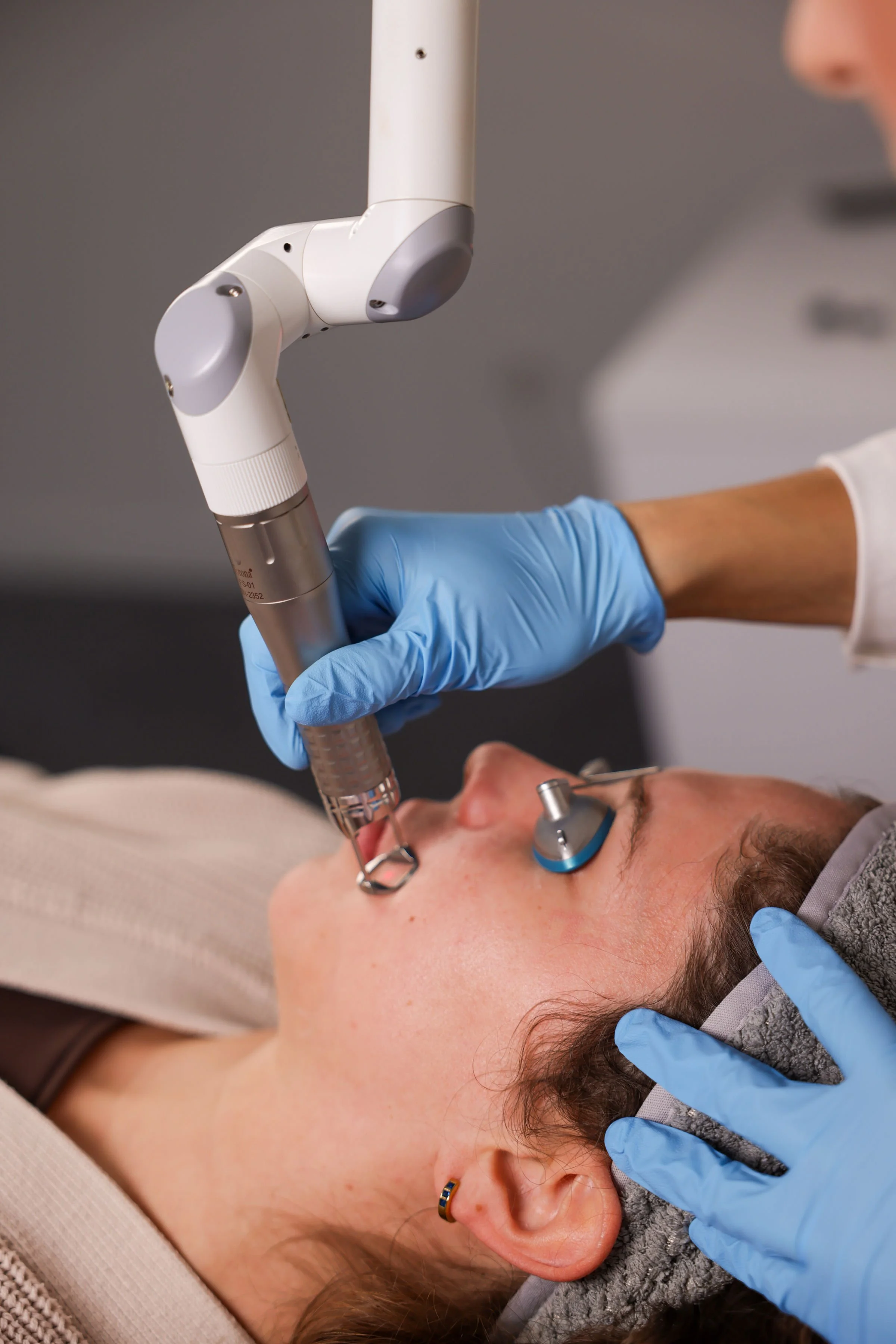 A person receiving a dental procedure using a dental drill, with a dental professional wearing blue gloves and a face mask, in a dental clinic.