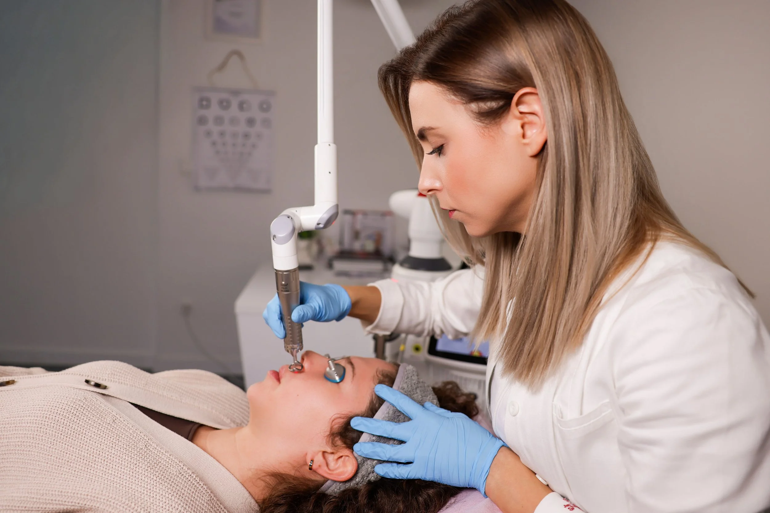 A medical professional performing a cosmetic procedure on a patient's face in a clinical setting.