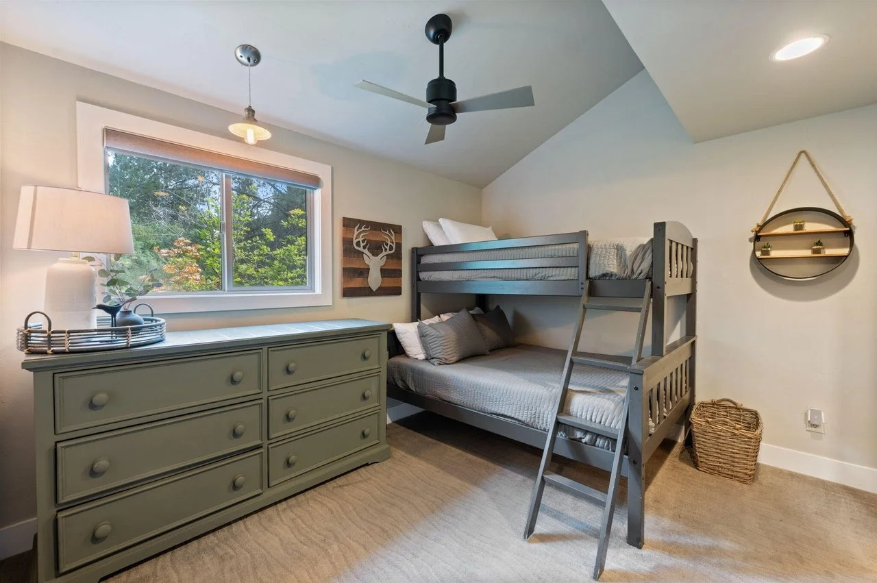 A cozy bedroom with a gray bunk bed, a dresser, a window, and minimal decor.