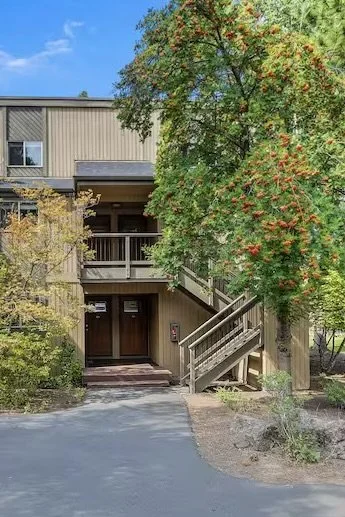 Exterior view of a residential building with a staircase, surrounded by trees and bushes, on a paved pathway.