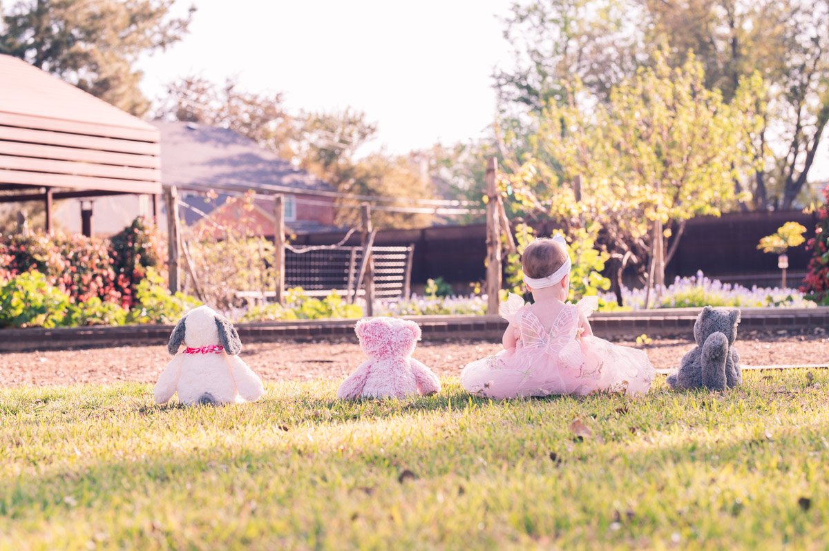 little girl sitting in grass with her stuffed animals