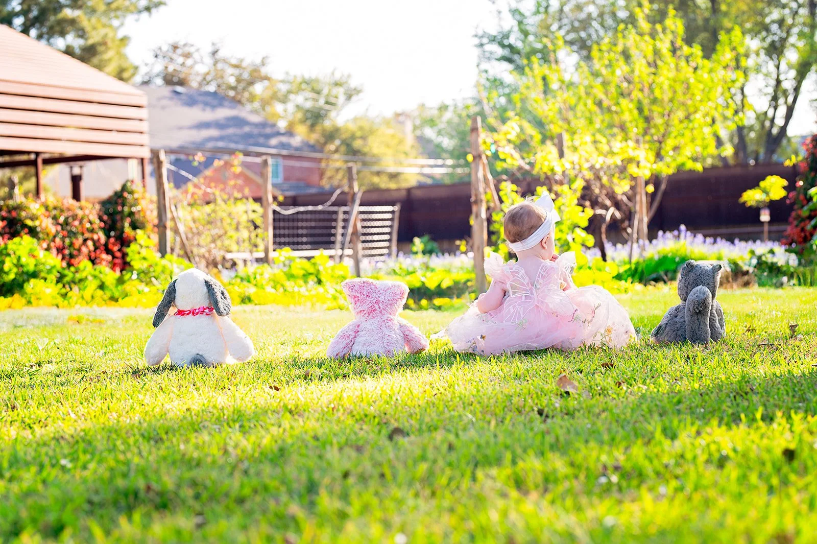 little girl sitting in grass with stuffed animals