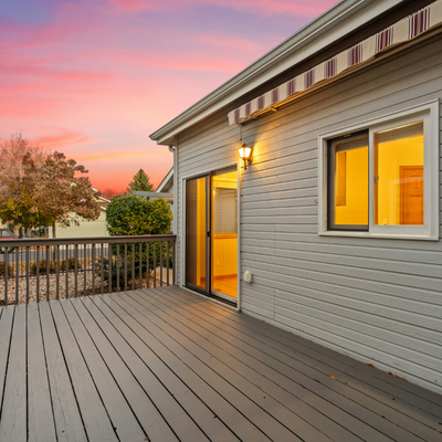 A residential house's outdoor balcony during sunset with a sliding glass door and warm interior lighting.