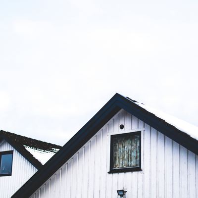 The upper part of a white house with a dark roof and a window, against a cloudy sky.