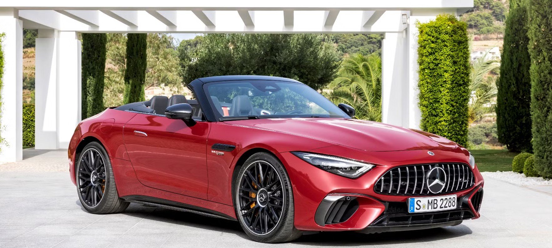 Red Mercedes-Benz convertible sports car parked outdoors with green trees and hedges in the background.