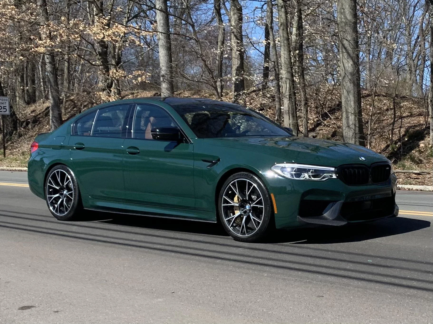 A green BMW sedan driving on a road with a wooded area in the background.