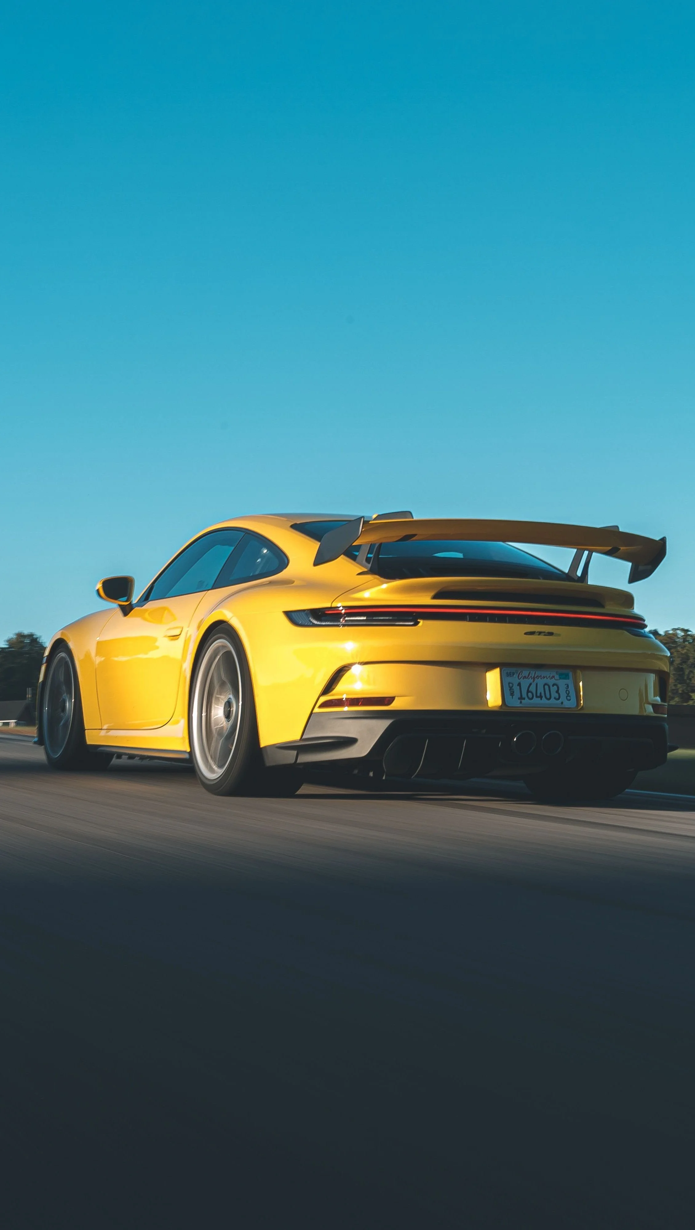 Yellow sports car driving on the highway with a blue sky above.