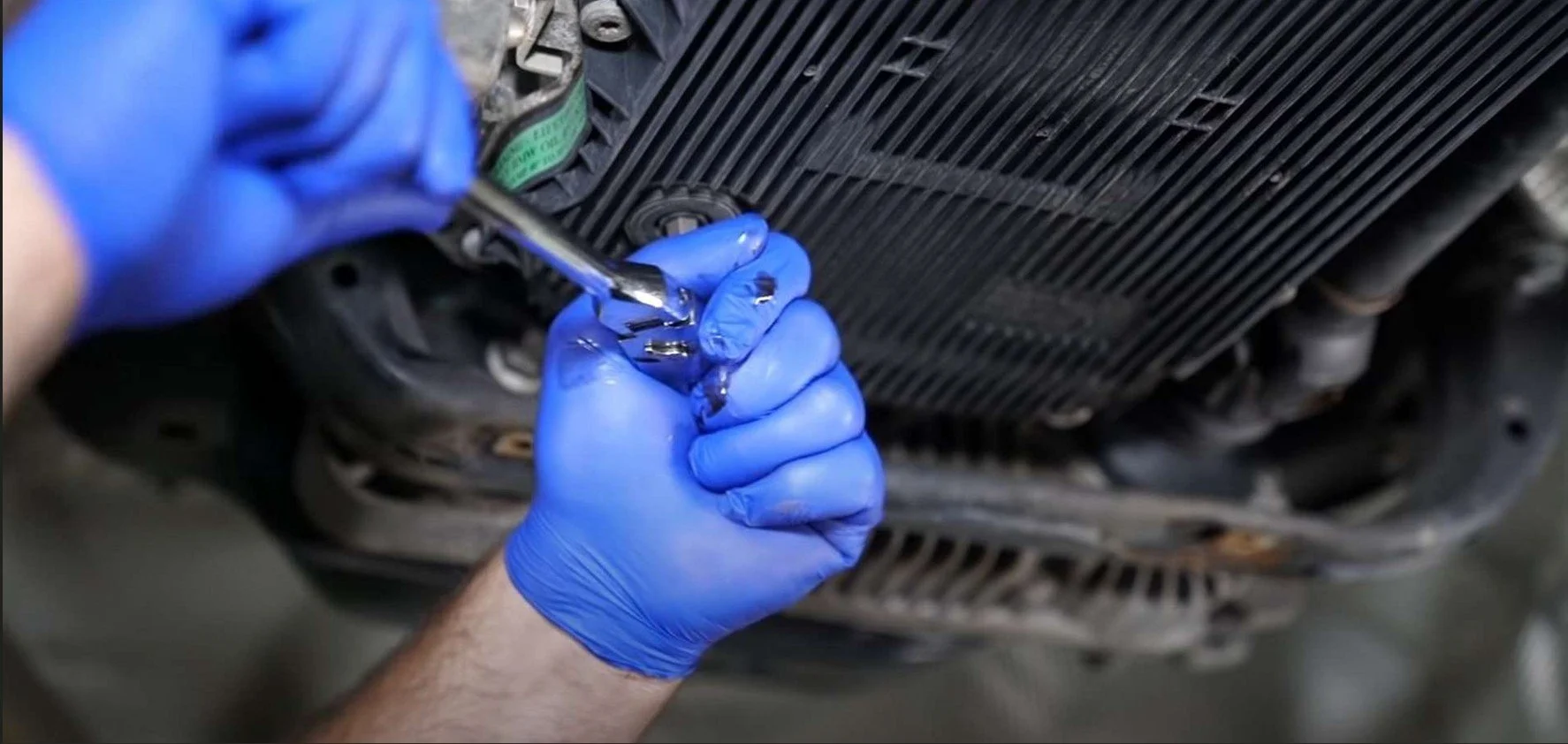 Person wearing blue gloves using a wrench to work on a vehicle's radiator or intercooler.