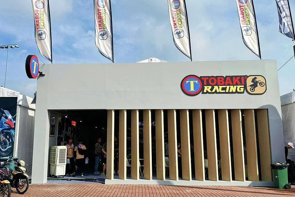 Exterior view of Tobaki Racing store with flags, motorcycles, and visitors inside.