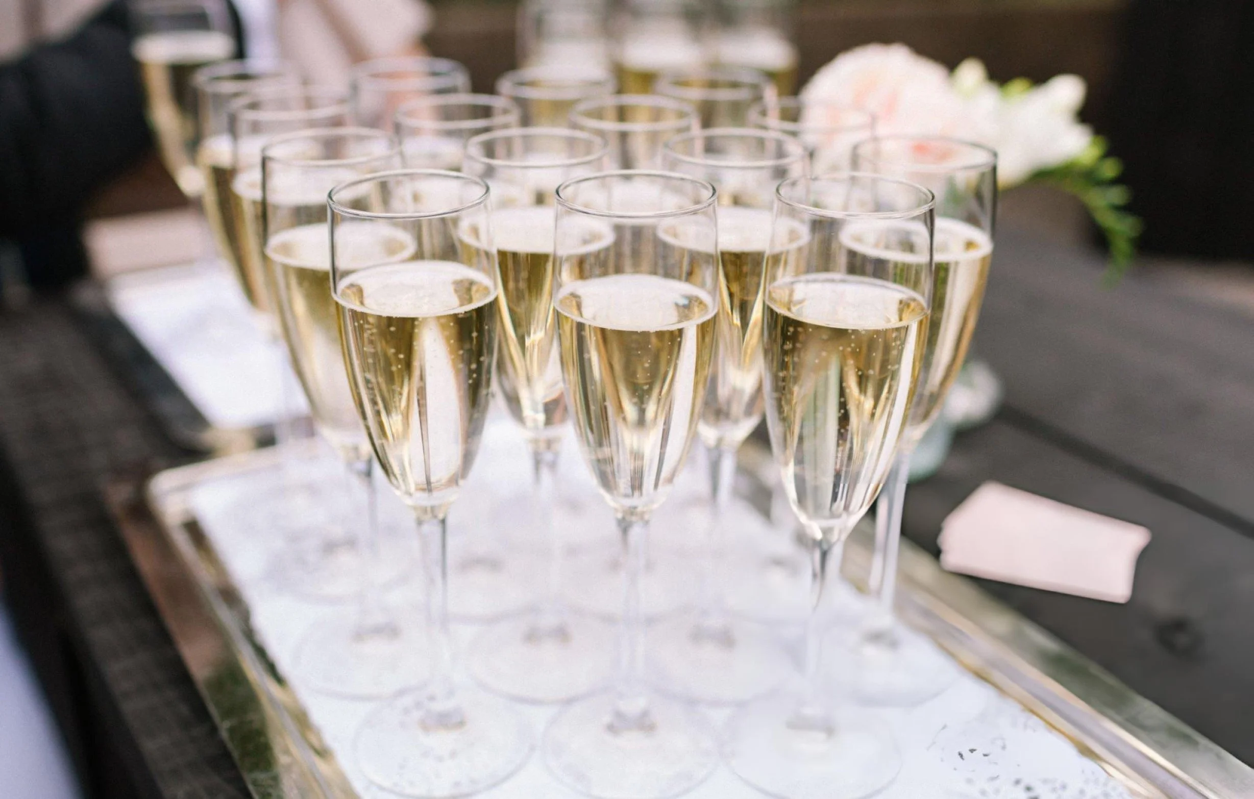Multiple champagne flutes filled with sparkling wine arranged on a white serving tray at a celebration or wedding event.
