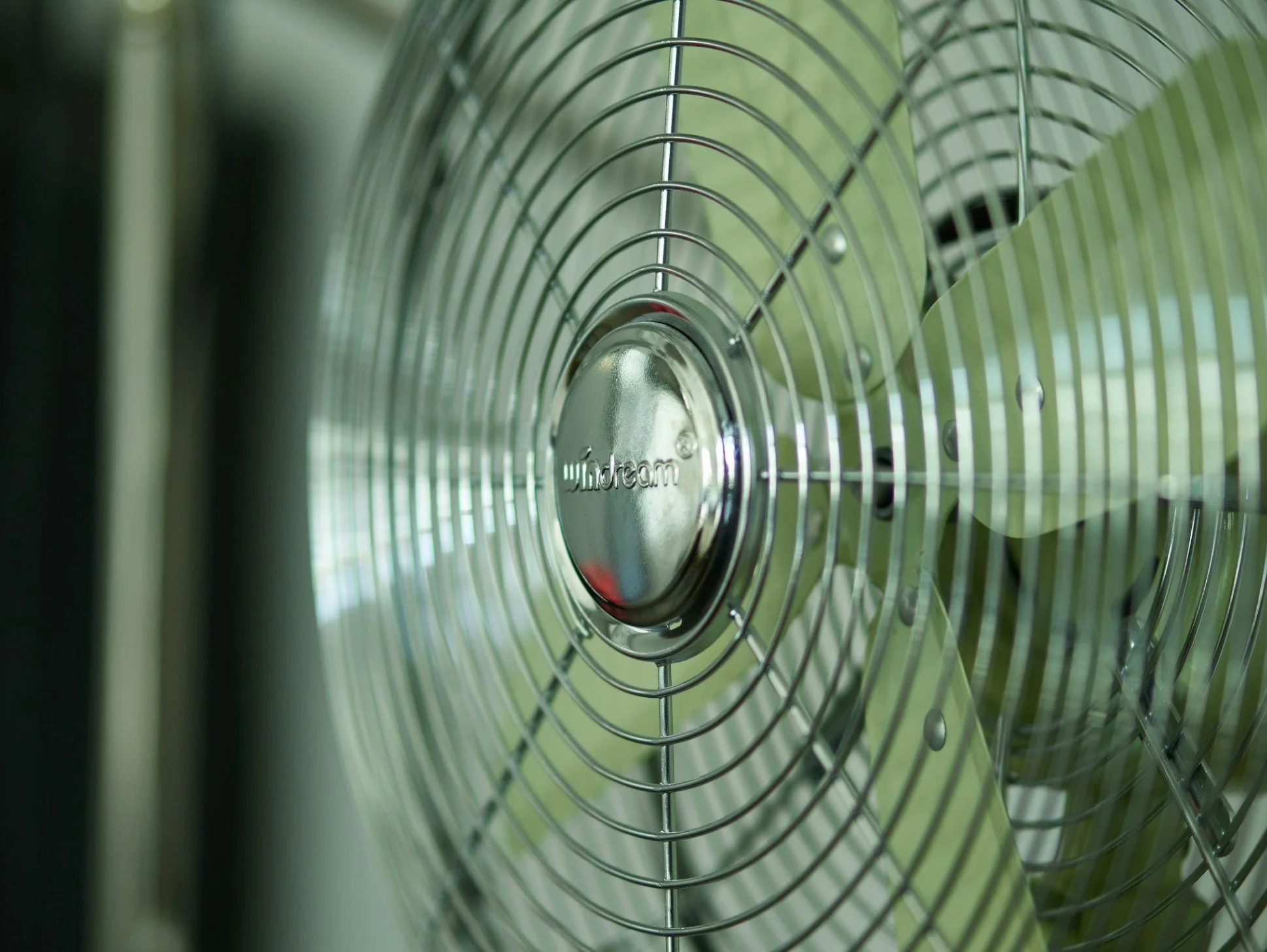 Close-up of a metallic electric fan with a protective grill and a central hub, likely part of a ceiling or large floor fan.