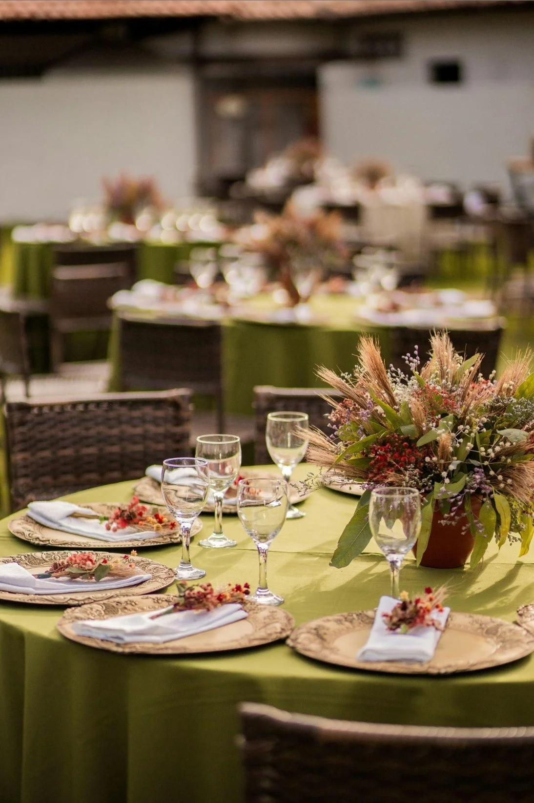 Decorated banquet table with floral centerpiece, wine glasses, plates with napkins, and a green tablecloth, set for an event in a large room.