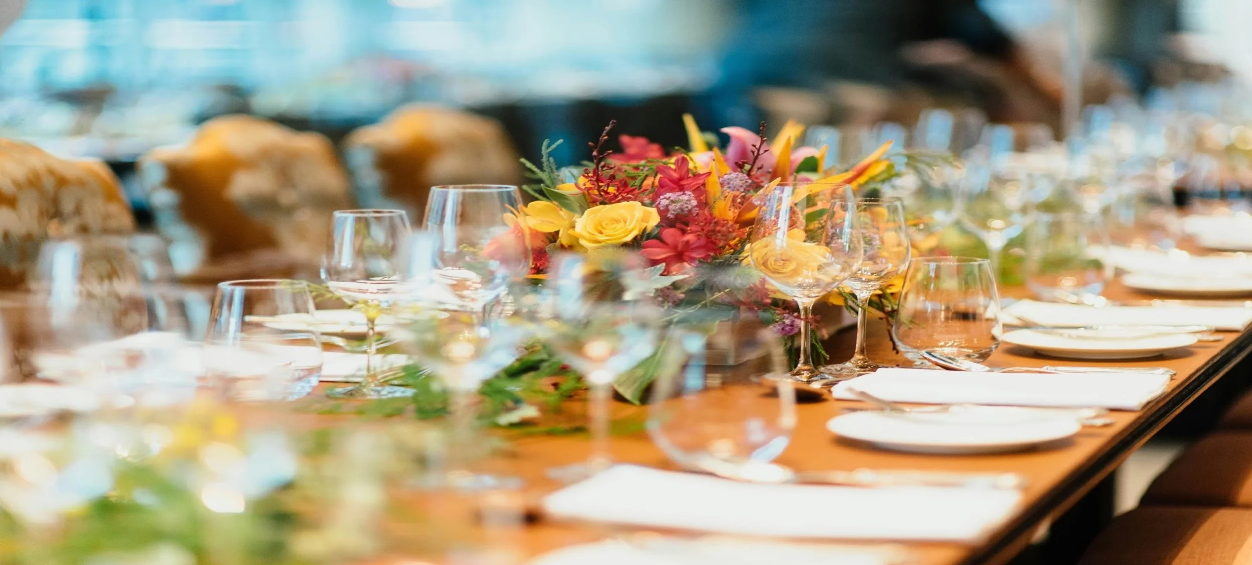 A close-up view of an elegant dining table setup with a colorful flower arrangement, wine glasses, and white plates, set for a formal event or celebration.