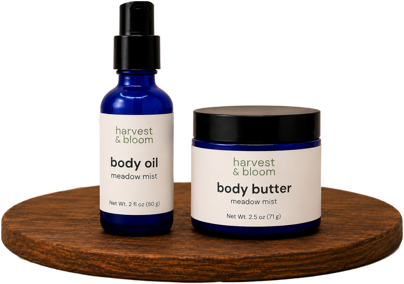 A glass bottle of body oil and a jar of whipped body butter by Harvest and Bloom on a round wooden riser, representing the natural body care line.