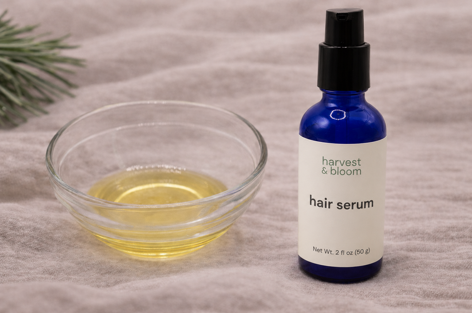 A close-up view of a clear glass bowl highlighting the golden, silky, and lightweight texture of a waterless botanical hair shine oil.