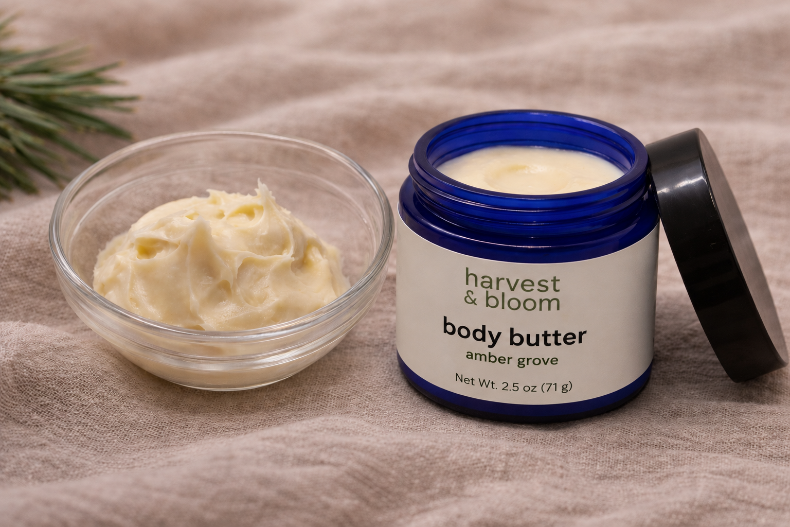 A small clear glass bowl holding a scoop of thick whipped tallow body butter next to an open blue jar of body butter.