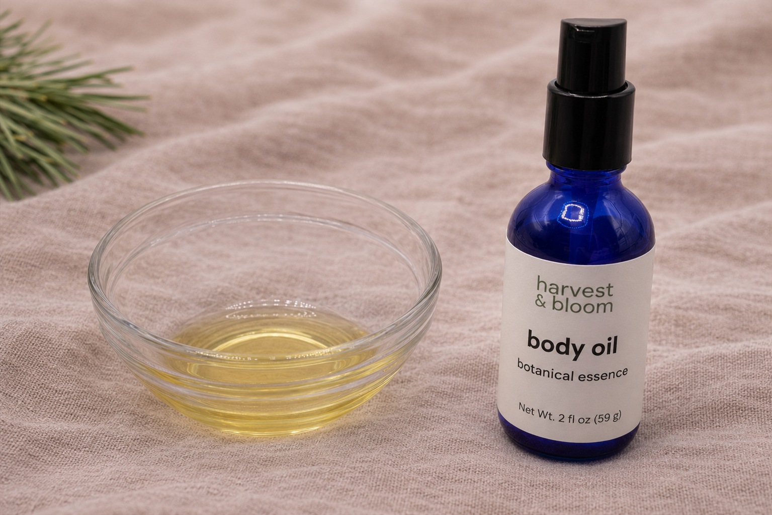 A clear glass bowl containing a golden, lightweight body oil next to a blue glass bottle, highlighting the silky, waterless, and fast-absorbing texture.