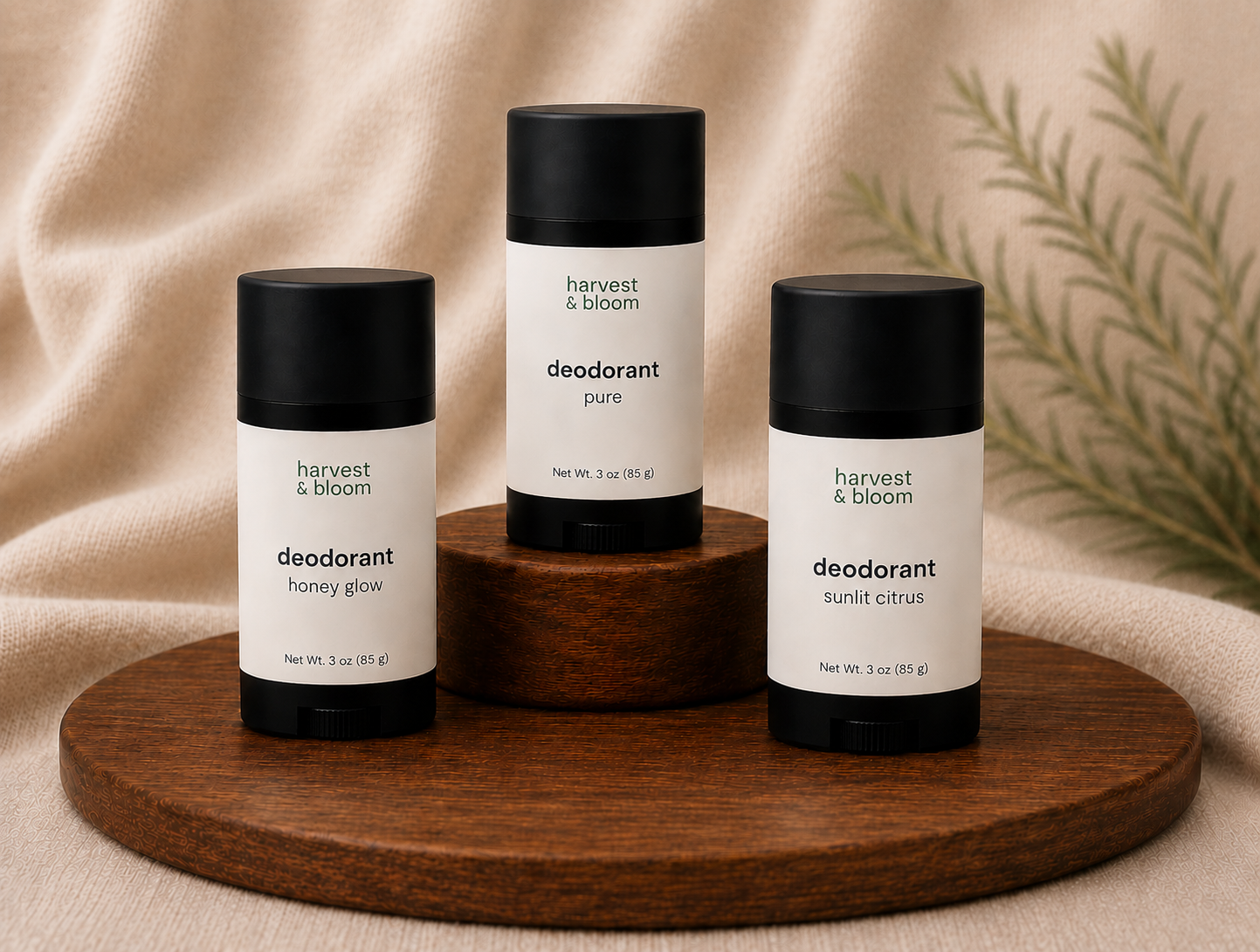 Three black twist-up tubes of Harvest and Bloom natural deodorant displayed on circular wooden risers against a soft fabric backdrop.