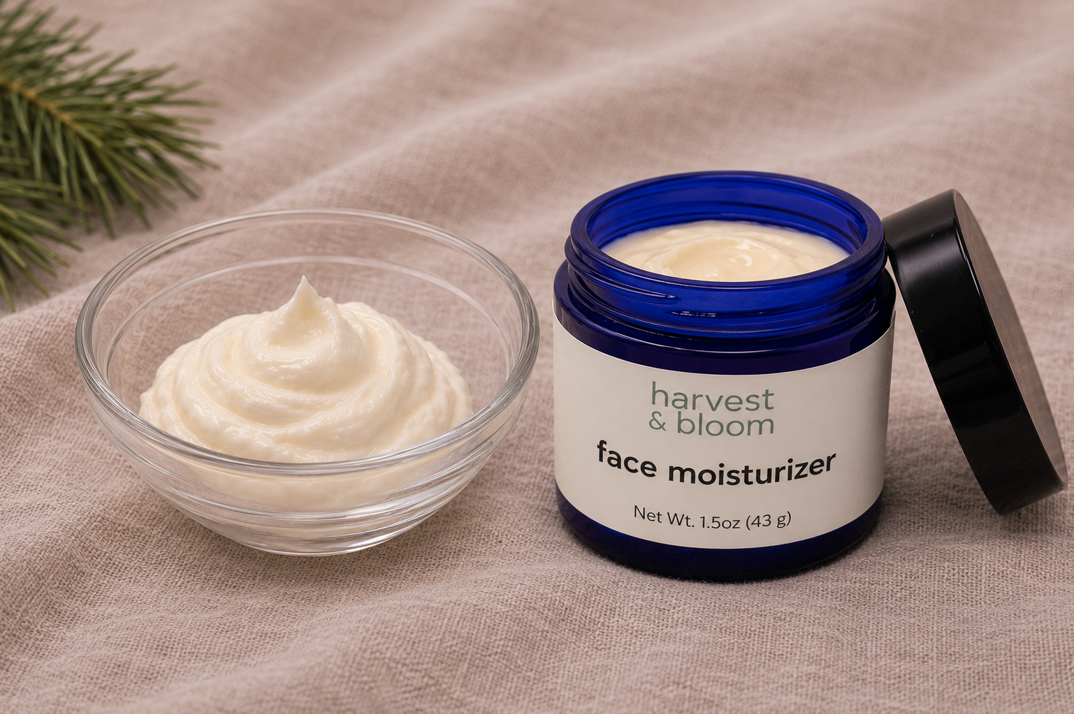 A close-up view of whipped, creamy face moisturizer in a small glass bowl alongside an open blue glass jar of Harvest & Bloom face moisturizer.