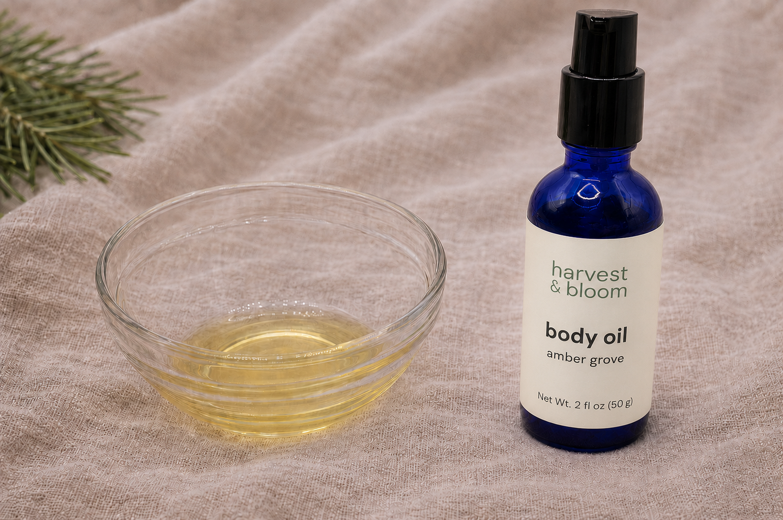 A close-up view of golden, lightweight natural body oil poured into a small glass bowl next to an individual cobalt blue glass pump bottle of Harvest & Bloom body oil.