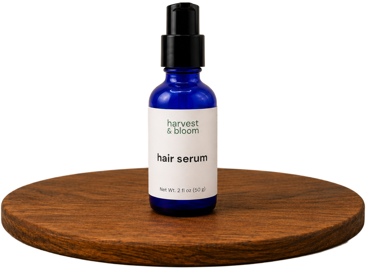 A cobalt blue glass pump bottle of Harvest & Bloom botanical hair serum for frizz control and shine, displayed on a round wooden riser.