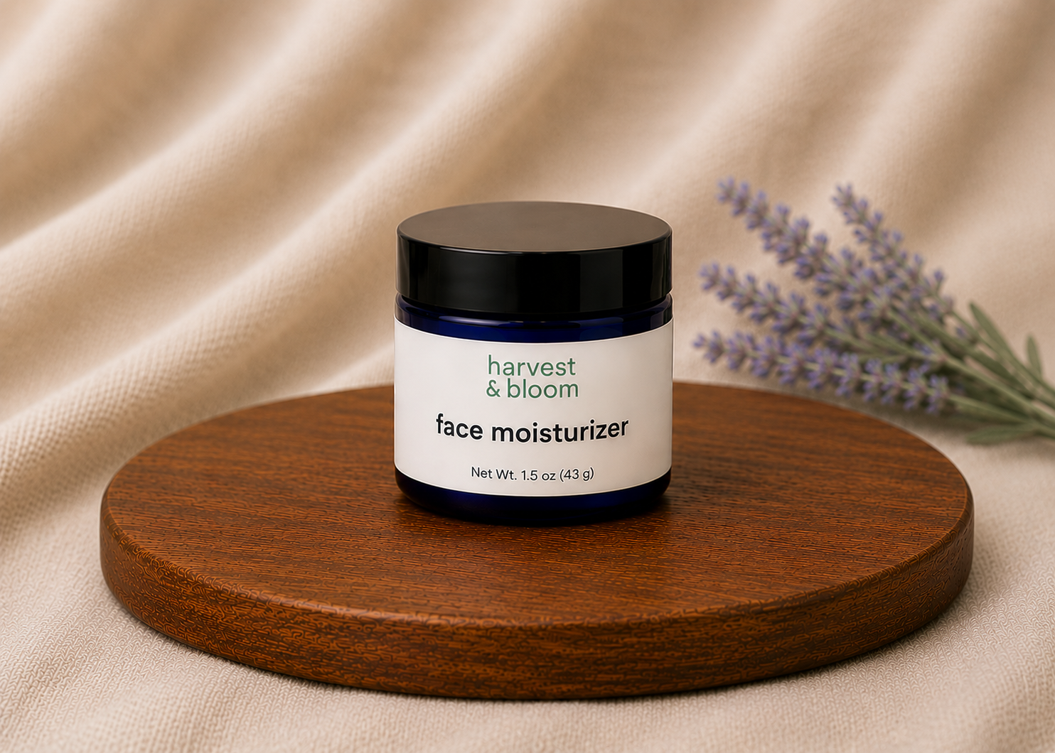 A single cobalt blue glass jar of Harvest & Bloom natural face moisturizer sitting centered on a round wooden tray over a draped soft linen background with lavender.
