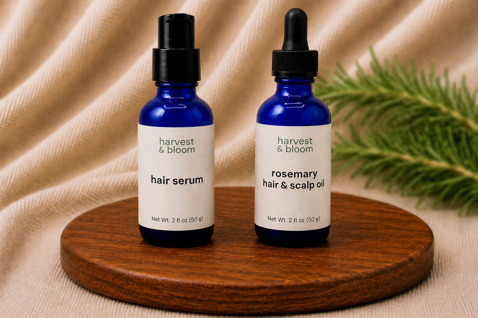 A Haircare Set by Harvest & Bloom featuring a cobalt blue glass bottle of hair serum and a rosemary hair and scalp oil bottle side-by-side on a round wooden tray over a soft linen background.