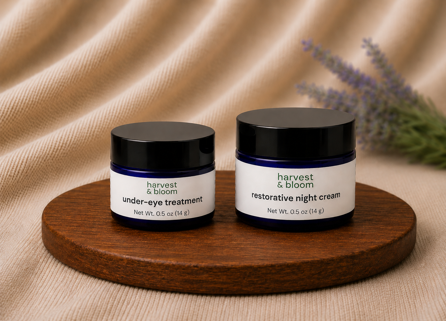 An Evening Skincare Set by Harvest & Bloom featuring a cobalt blue glass jar of under-eye treatment balm and a restorative night cream jar side-by-side on a round wooden tray over a soft linen background.