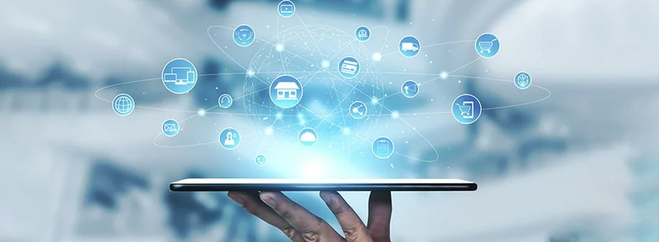 Una mano sostiene una tableta con íconos digitales que representan tecnologías conectadas, viviendas, comercio y comunicación en un fondo difuso.