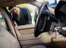 Person in a suit looking into the open driver side door of a car, with keys hanging from the ignition.