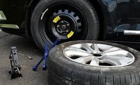 Car tire being changed with a ratchet wrench and a blue tool on the ground.