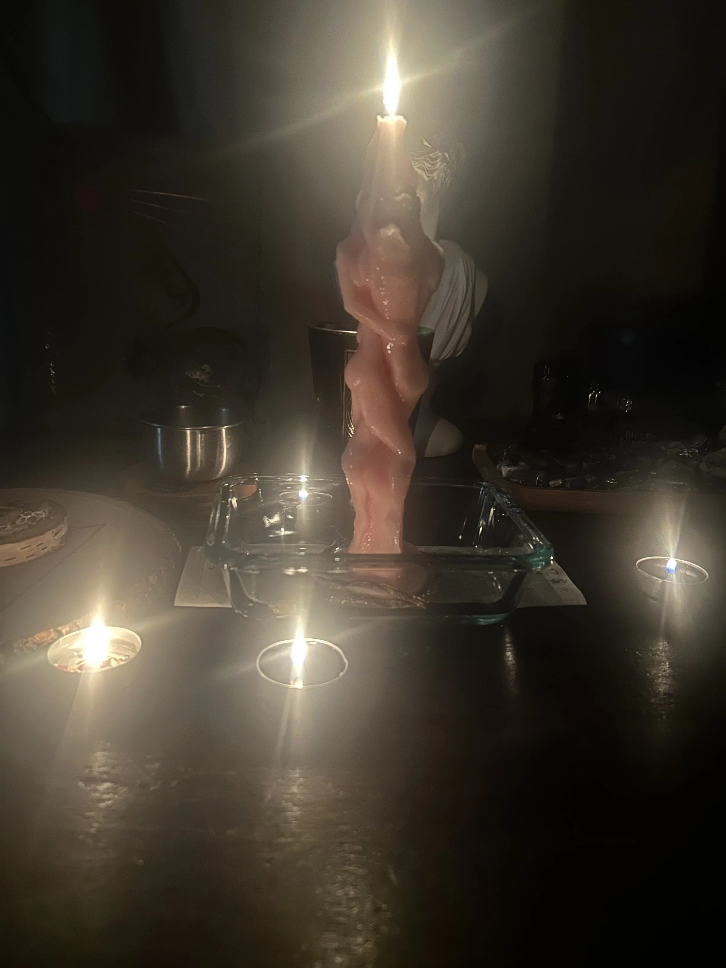A person is holding a lit spiritual candle on top of a twisted piece of raw chicken or meat, surrounded by small candles on a dark table.