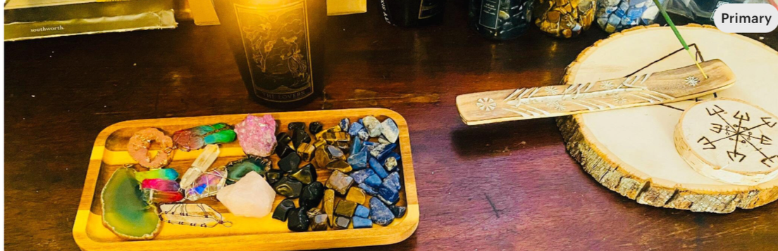 A wooden tray with various colorful crystals and jewelry pieces on a dark wooden table.