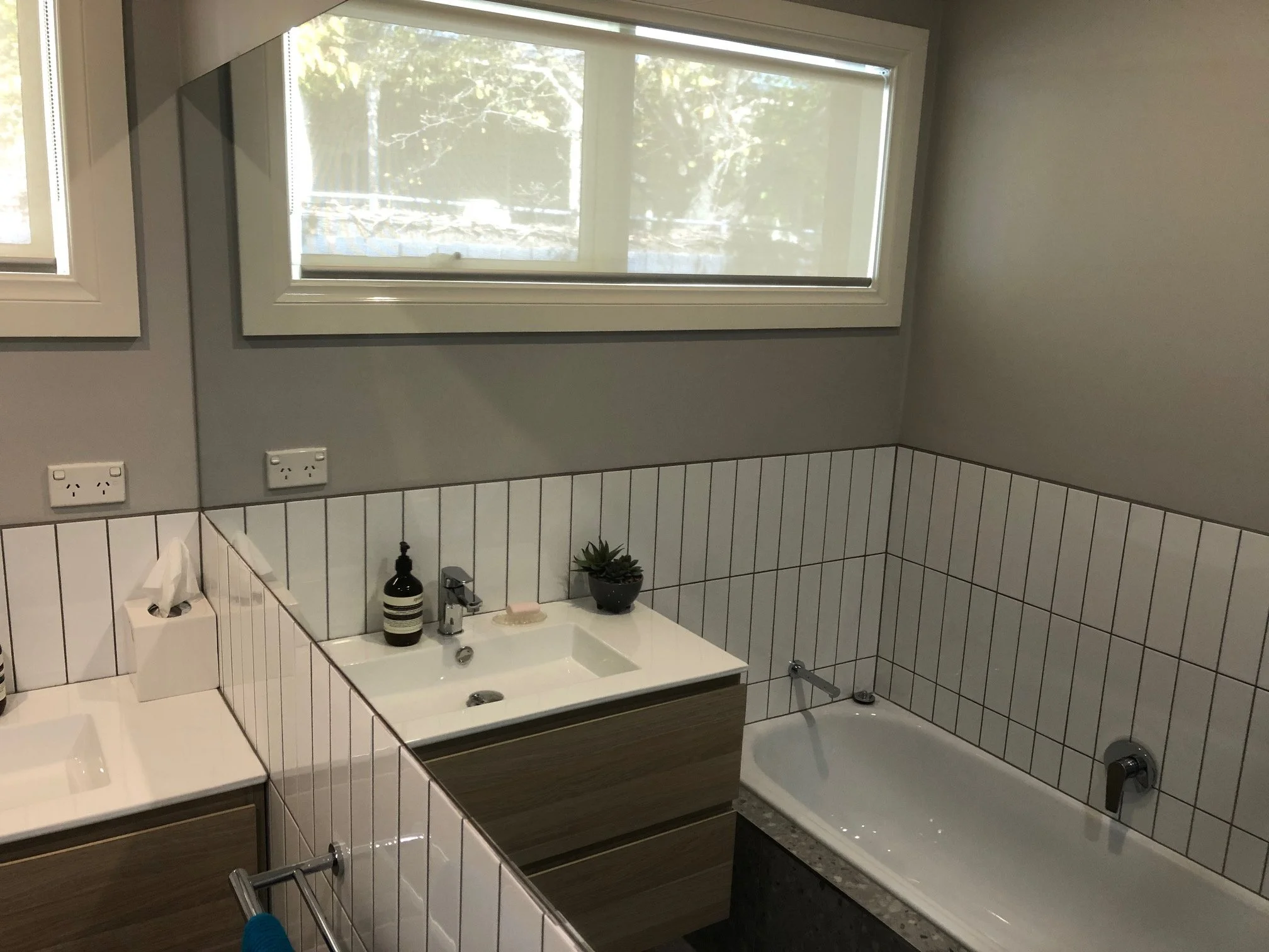 Modern bathroom with tiled walls, floating vanity, sink, bathtub, frosted window.