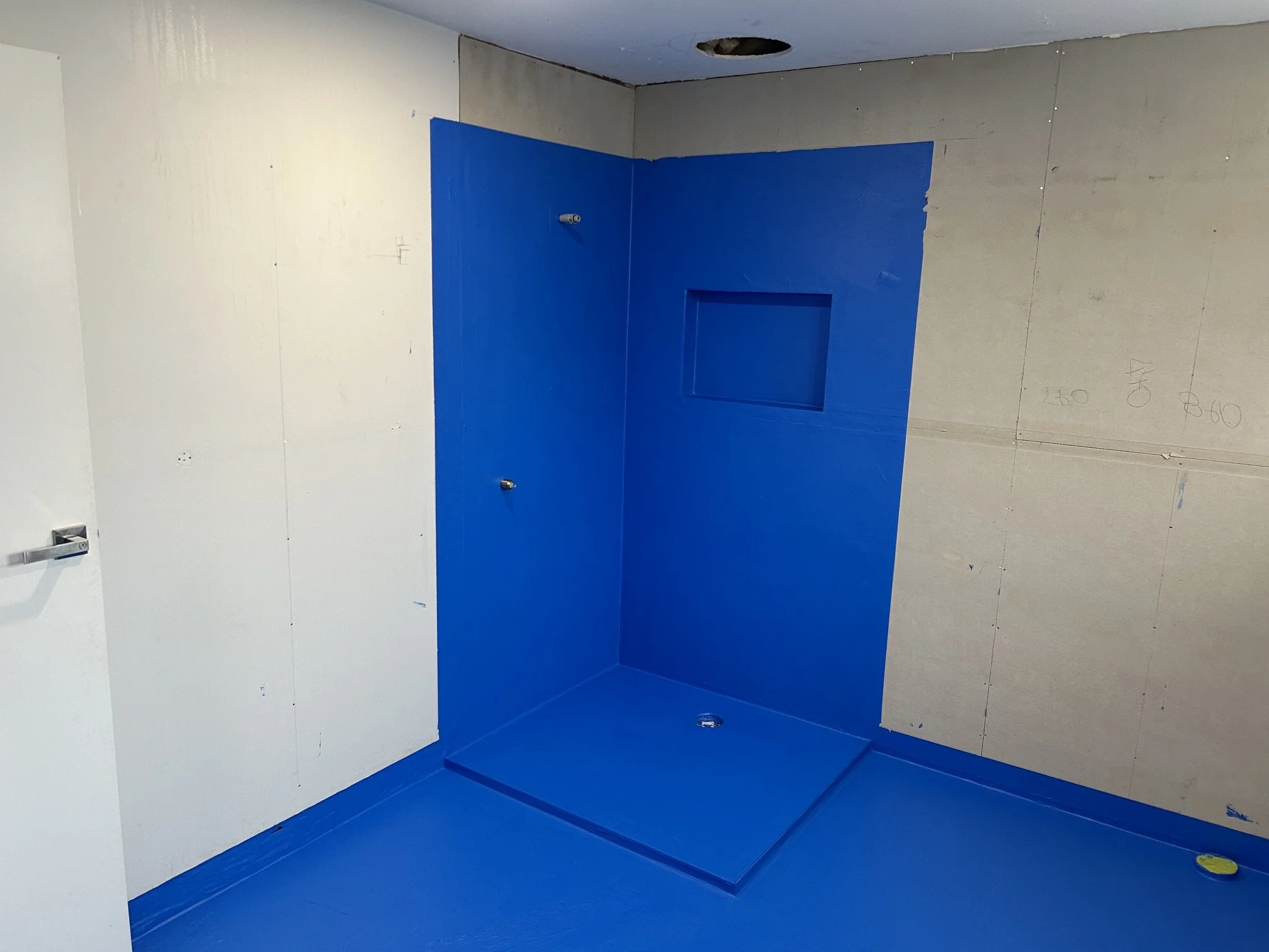 Unfinished bathroom with a bright blue waterproof shower enclosure, installed plumbing fixtures, and exposed drywall.
